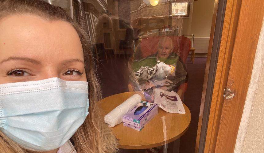 Jen, wearing a mask, visiting her dad at the care home, behind a screen