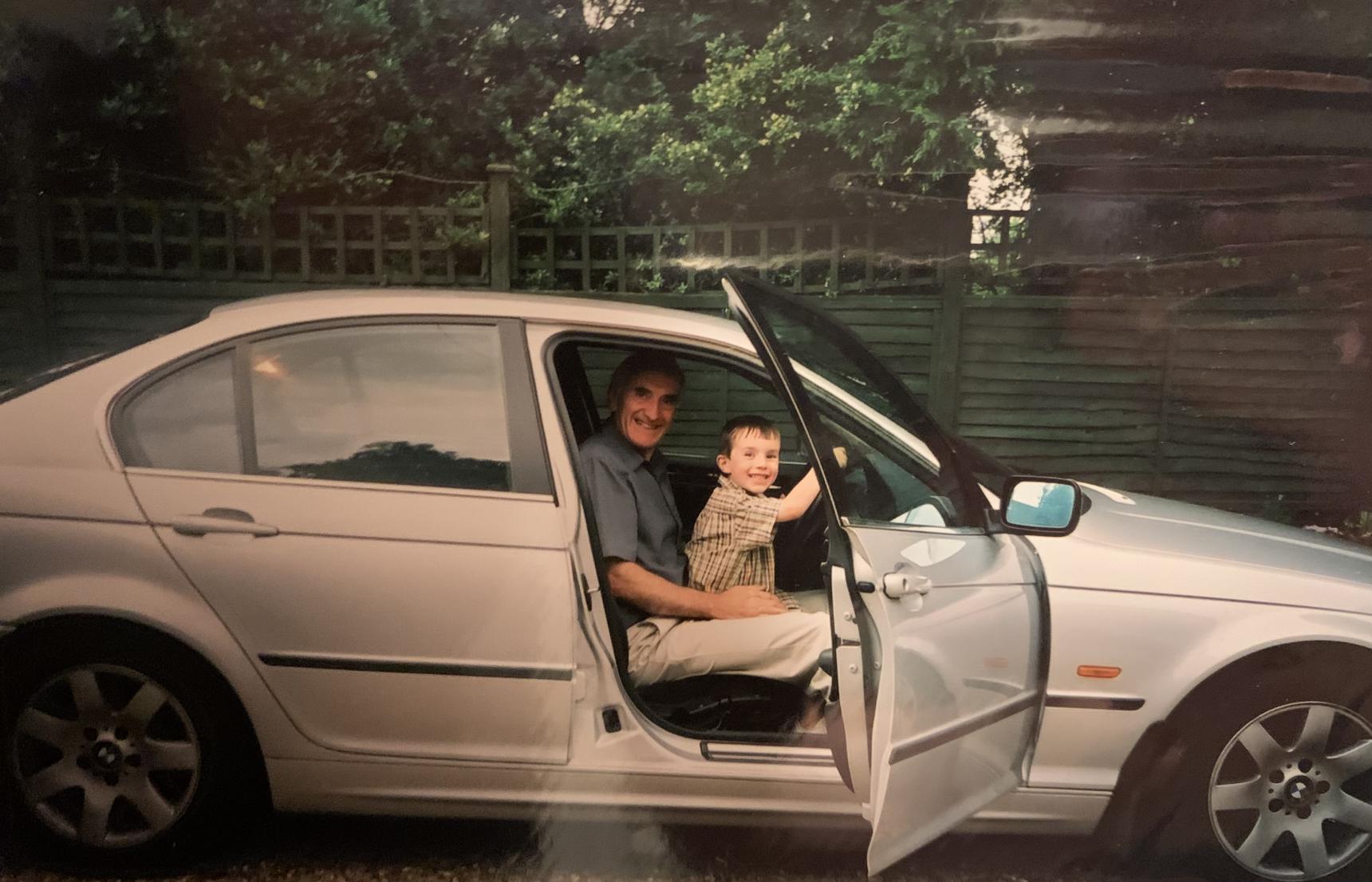 Tom as a young boy on his Grandad's knee, steering his car