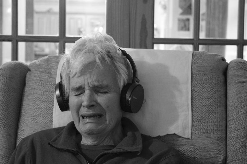 Kyra's grandma, Winifred, sits in an armchair listening to music through headphones and crying
