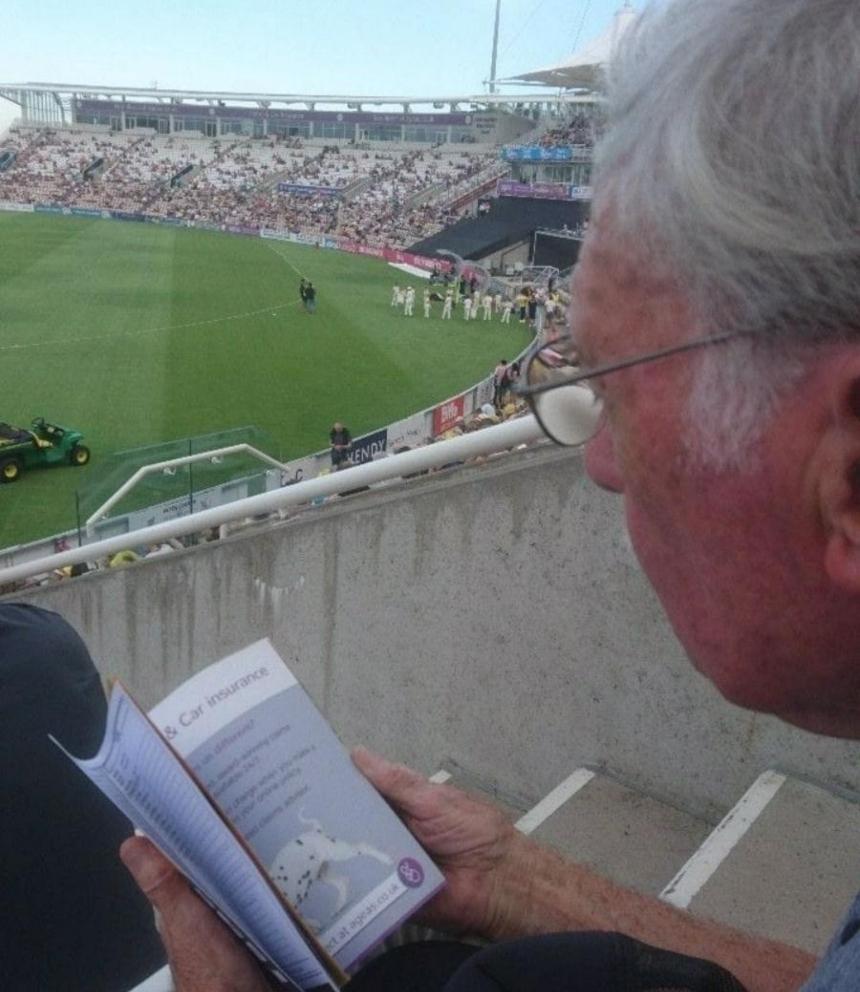 Stan sitting in the stands at Kent vs Hampshire in 2018, reading a programme