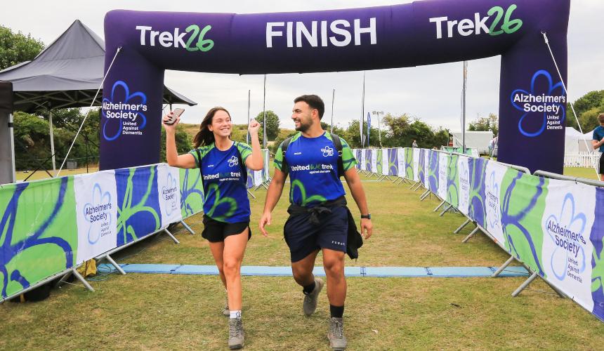 Vicky and Ercan smiling and wearing Trek26 shirts while under the Trek26 finish line and cheering