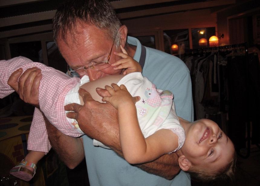 An old photograph of Sophia as a toddler, being held by her Papa who is blowing on her stomach to make her laugh