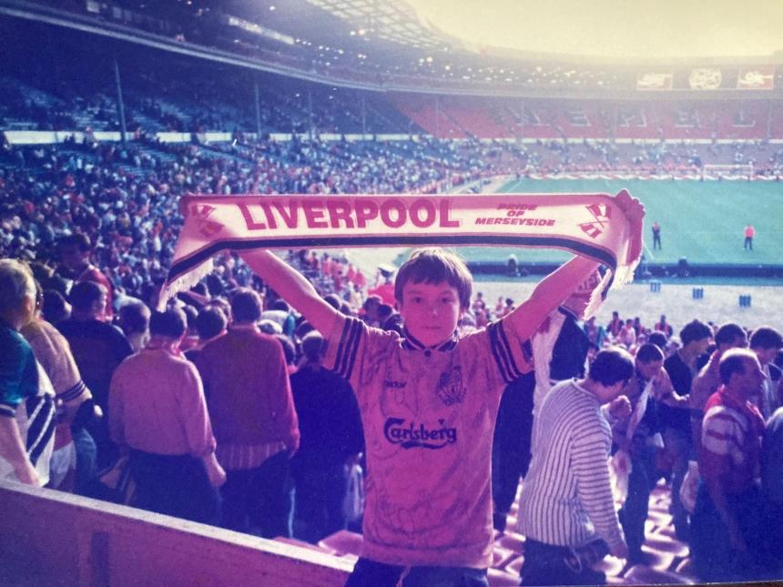 An old photograph of Bob's grandson holding Liverpool F.C. scarf above his head at Wembley stadium