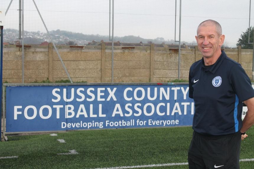 Paul Saunders stood in front of a sign that reads 'Sussex County Football Association: Developing Football For Everyone'