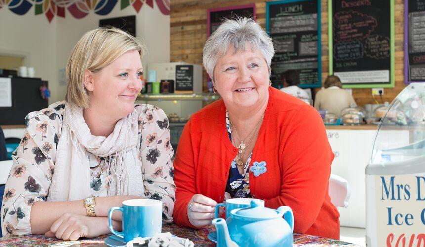 Two people sit in a cafe with mugs and a teapot