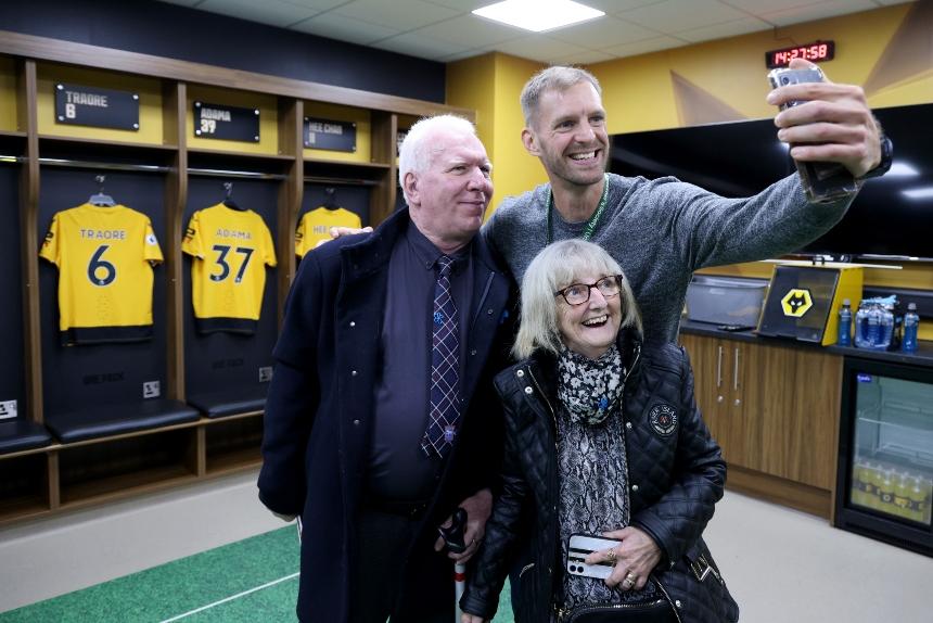 Peter and a woman pose for a picture that an Alzheimer's Society employee is taking on their phone, in the Wolverhampton F.C. dressing room 