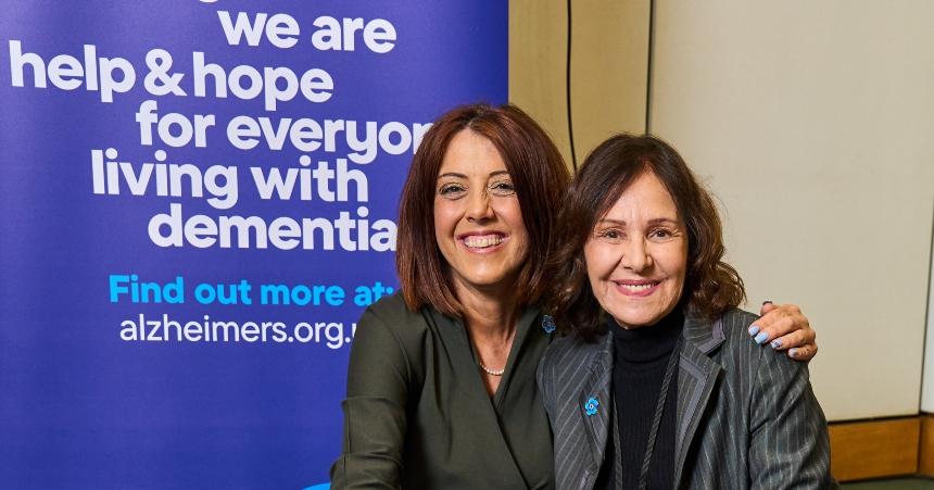 Dame Arlene Phillips and Alzheimer's Society CEO Kate Lee posing for a photograph in front of an Alzheimer's Society branded board