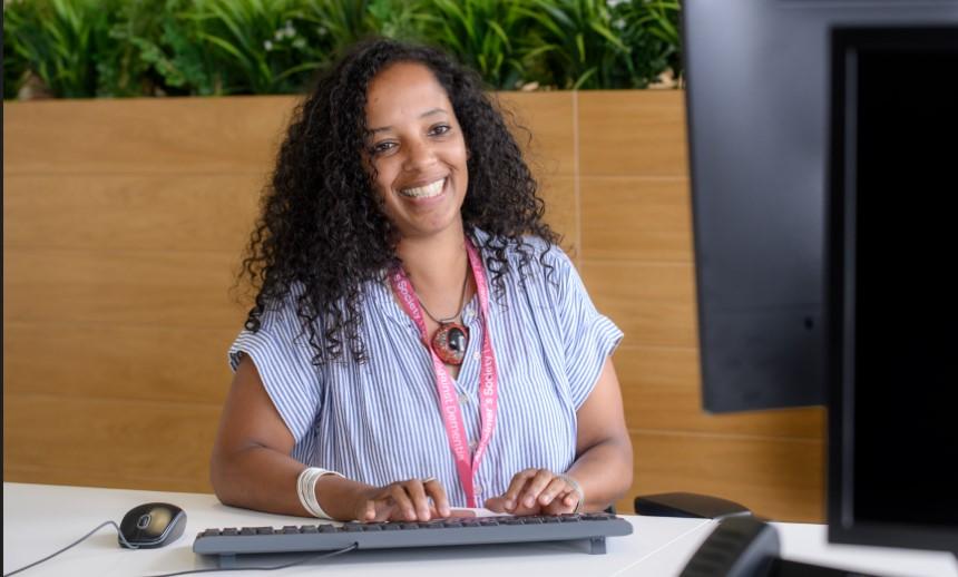 A person sits at  desk smiling in front of a computer