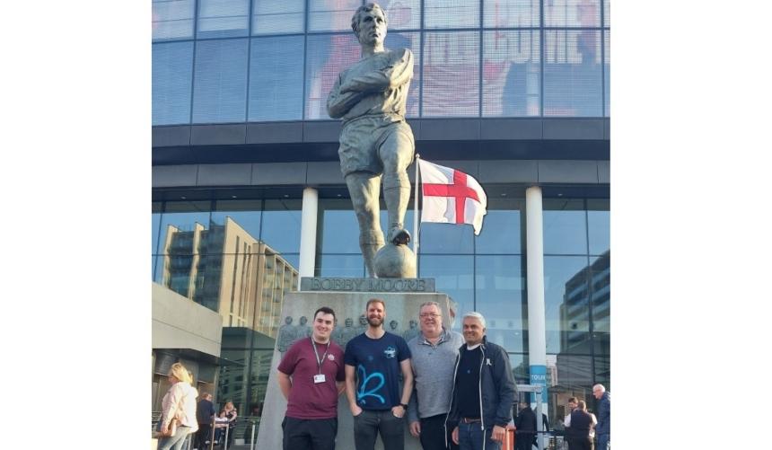 Sport united against dementia members standing in front of a Bobby Moore statue