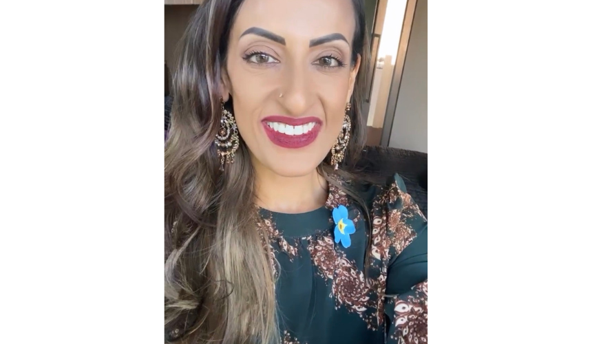 Dr Karan Jutlla taking a picture, wearing traditional South Asian clothing and a forget me not pin badge