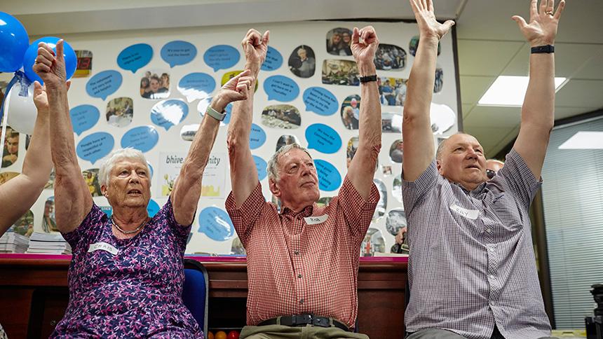 Three people affected by dementia try seated exercises at the Feel Good Folder launch