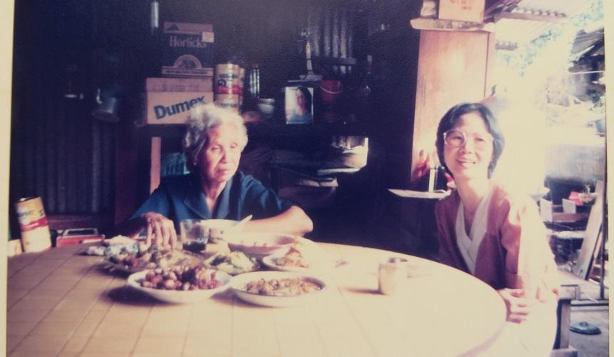A vintage photo of Ai Lyn (right) with her mum (left) sat at a table with food