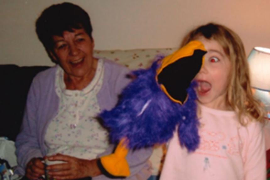 Grace as a child with a bird plushie as her Nanna laughs in the background