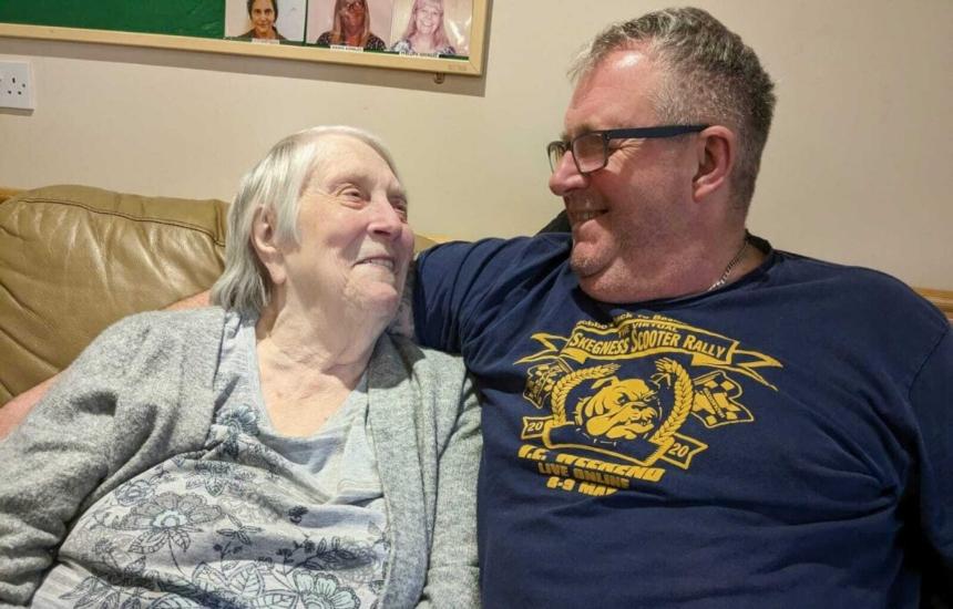 Peter and Doreen smiling, sat close together on a sofa