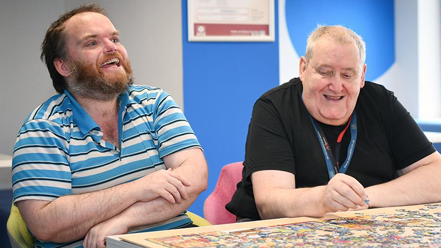 Adam and Bob Joesbury sit together at a table. They are laughing and completing a jigsaw.