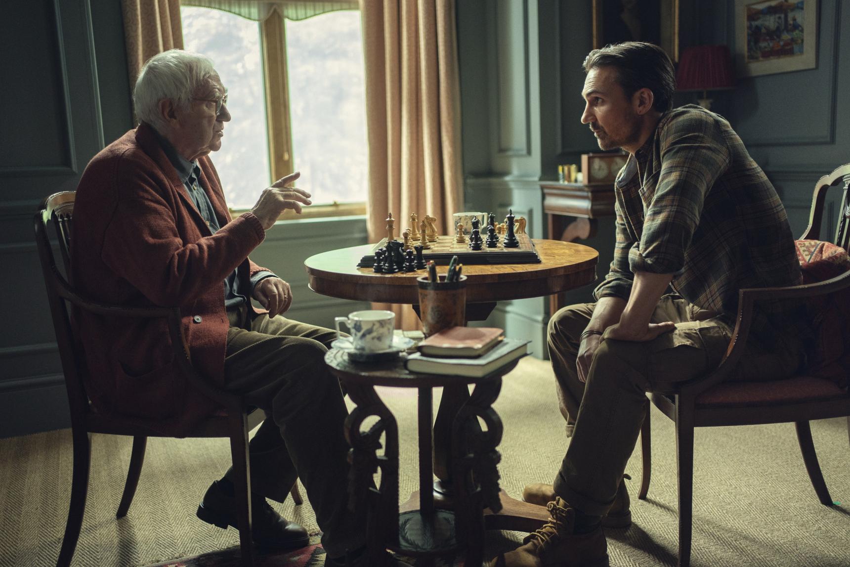 An older man and younger man play chess while seated