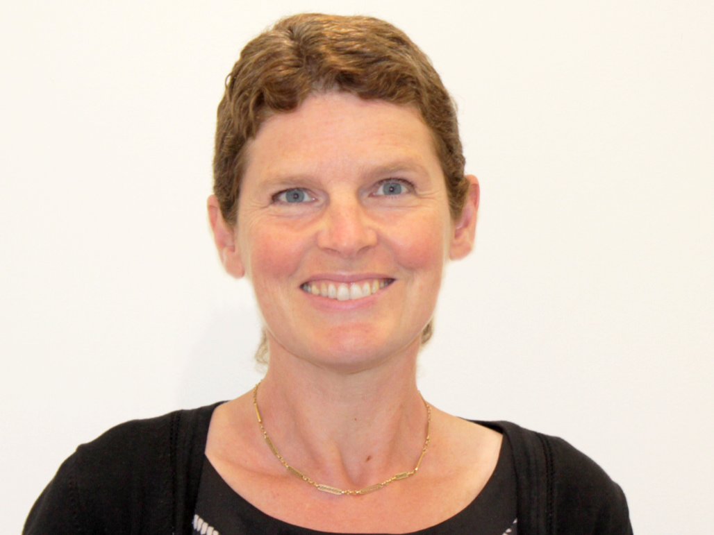 A woman with very short brown hair, smiling and wearing a black top