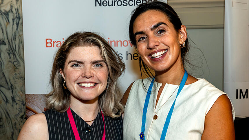 A woman with short blonde hair wearing a striped black vest and another woman with black hair wearing a white vest