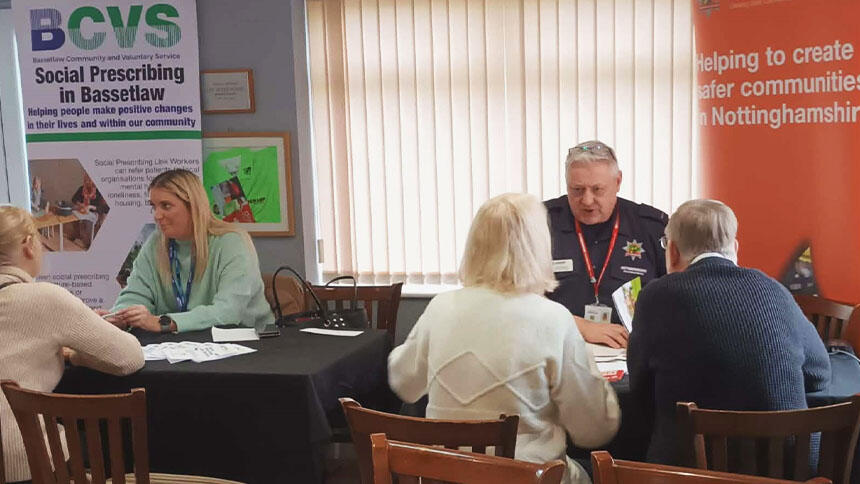 A couple sat at a desk talking to a man, there is also a person in the background speaking to someone else at a desk.