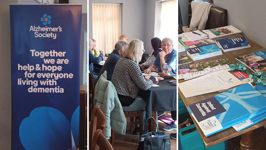 A table of Alzheimer's Society booklets at the support hub, an Alzheimer's Society banner and people sat at tables talking to each other. 