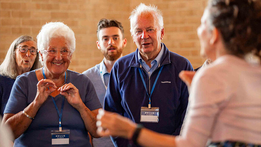 Man and woman wearing blue and watching a choir leader, behind them is another man and woman
