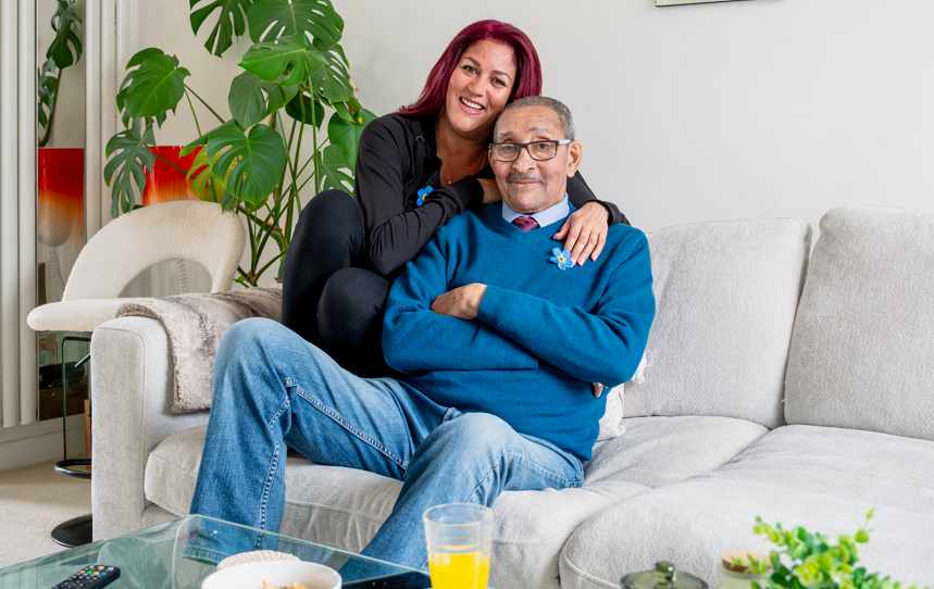 An younger woman hugs and older man while sat together on a grey sofa