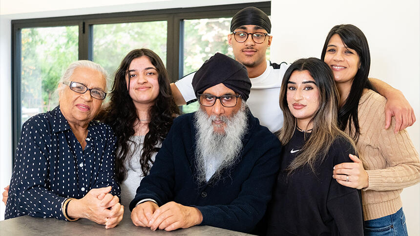 Harjit Singh Sagu sat at a table, surrounded by family - his wife and some of their children and grandchildren