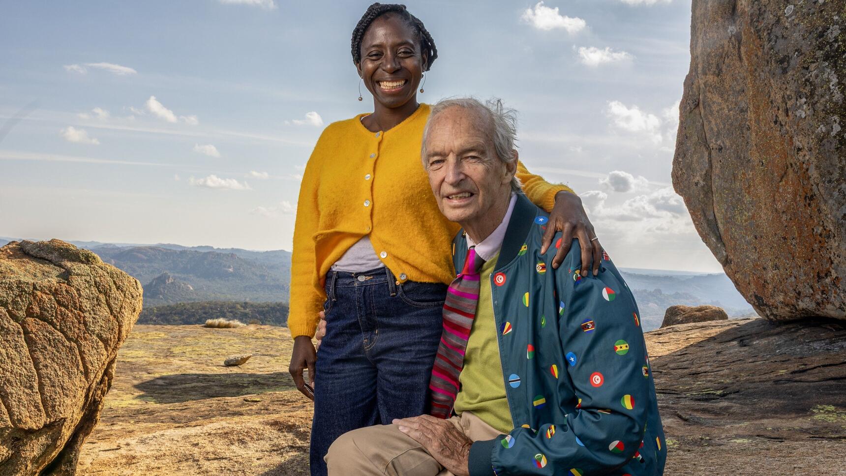 A man sat on a rock hugged by a standing woman in a sandy landscape