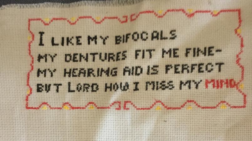Keith Day's cross stitch which reads 'I like my bifocals, my dentures fit me fine, my hearing aid is perfect, but Lord how I miss my mind'.