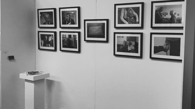 Kyra's photography exhibition, featuring 9 photographs displayed on a white wall, with a small podium