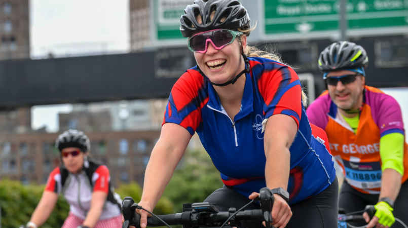 Woman cycling past road sign, smiling, at Ride London