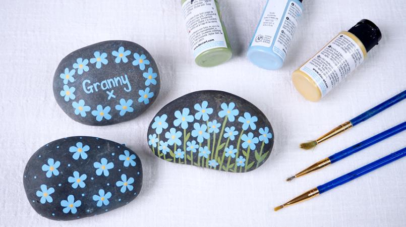 three grey stones with blue forget-me-nots painted on them