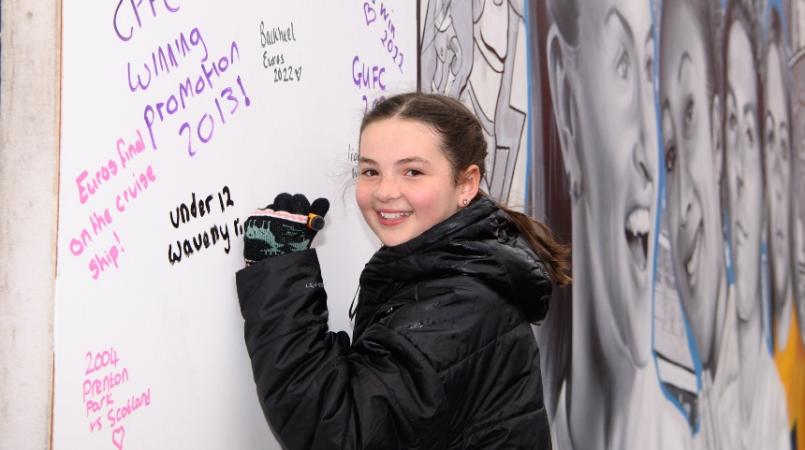 A fan writing on the Lionesses mural outside Brentford stadium