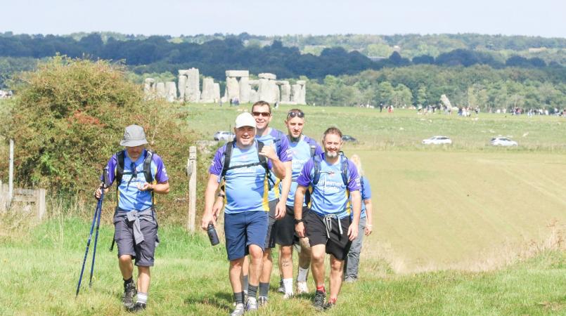 A group of 3 trekkers walking with Stonehenge in the background