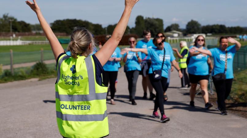 Volunteer in high vis with arms up, cheering at walkers waving