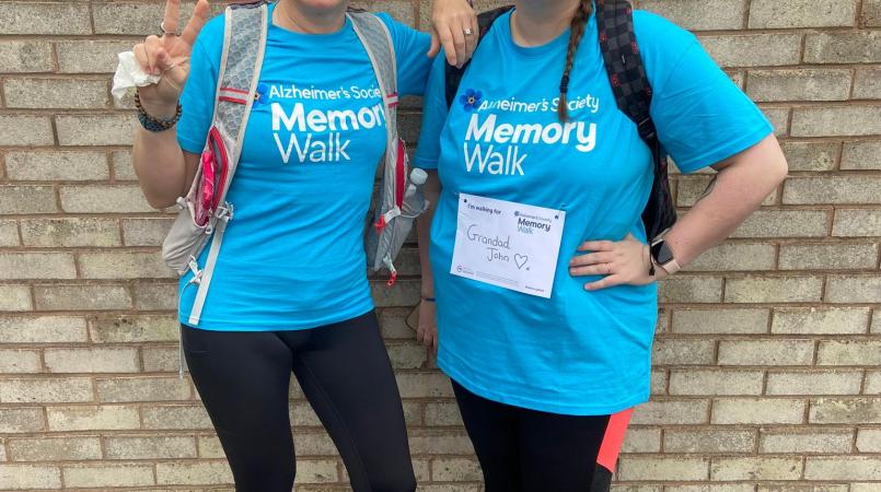 2 women arm in arm, smiling at the camera wearing blue Memory Walk t-shirts