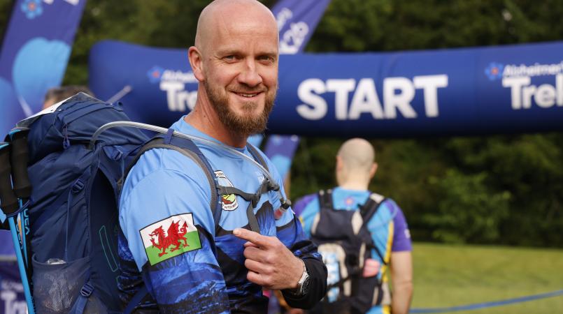 Man smiling and pointing to a Welsh flag on his arm.