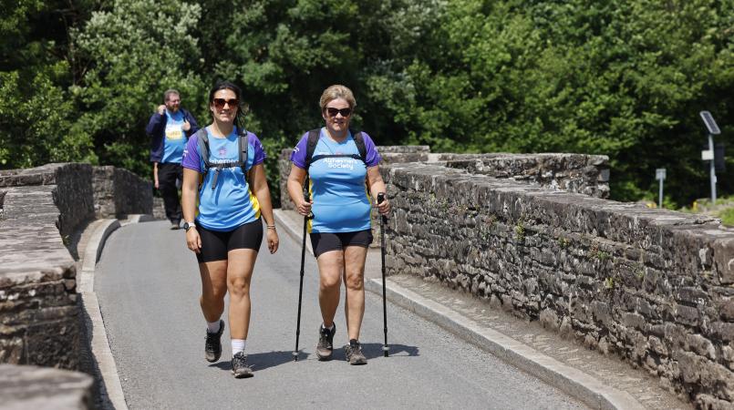 Two women walking on a countryside bridge.