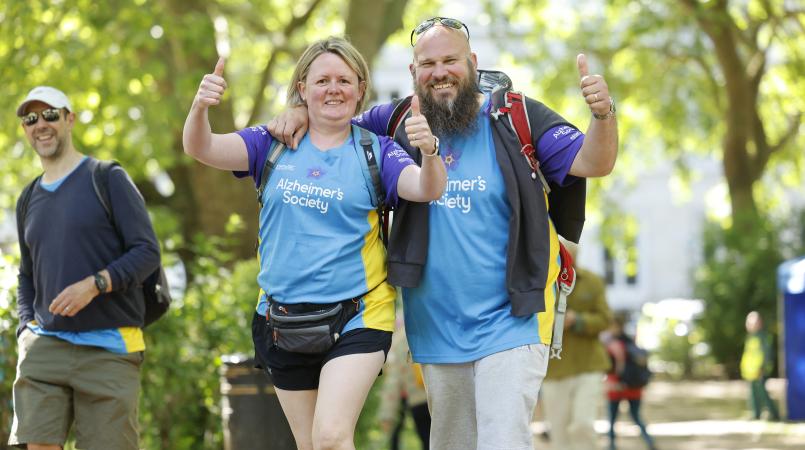 Couple with thumbs up walking through a park.