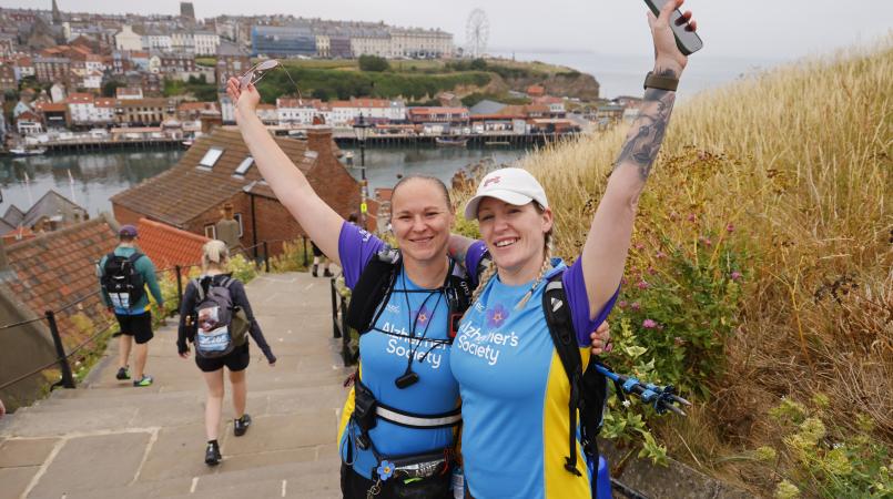 Two women posing at the top of stairs leading down to a seaside town.