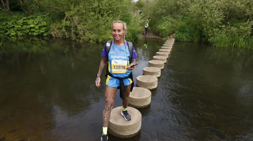 Woman crossing stepping stones over a river.