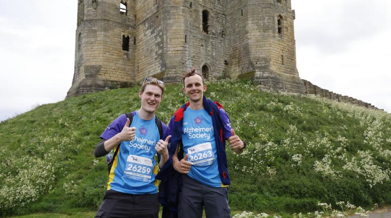 Two men smiling underneath a castle on a hill.