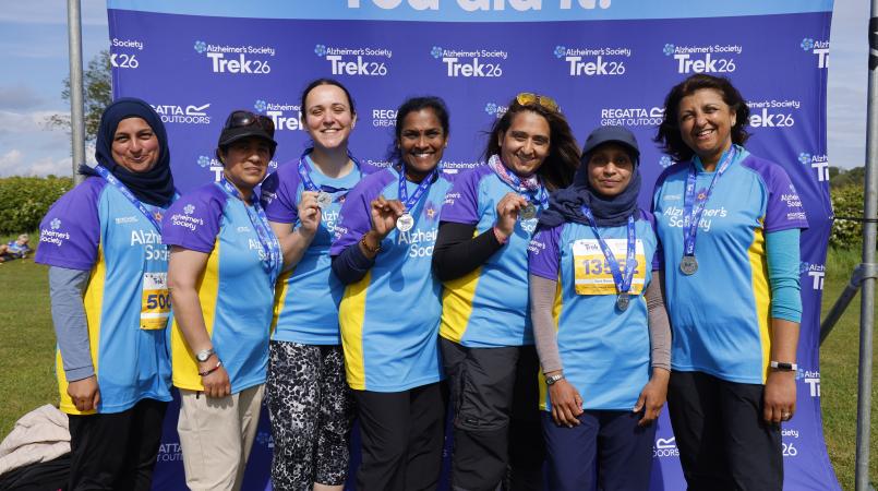 A group of women standing in front of a you did it sign with medals.