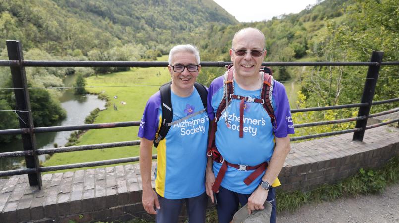 Two men smiling on a bridge in a valley.