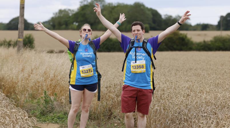 Two people with their arms raised walking through a field.