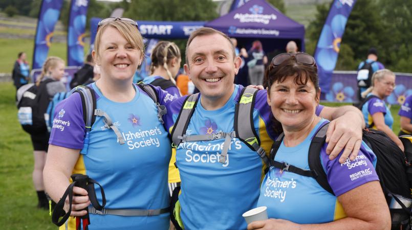 Group of people smiling in front of Trek26 tents and flags