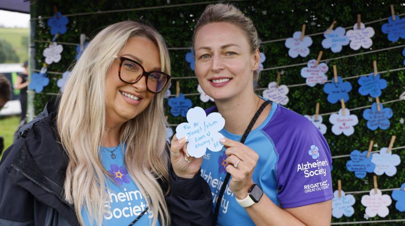 Two women holding a forget me not paper flower.