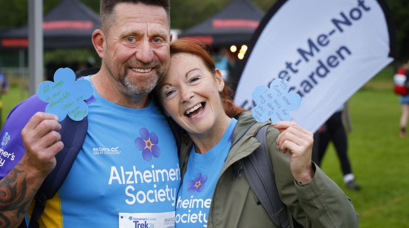 Couple posing in front of a forget me not flag with flowers.
