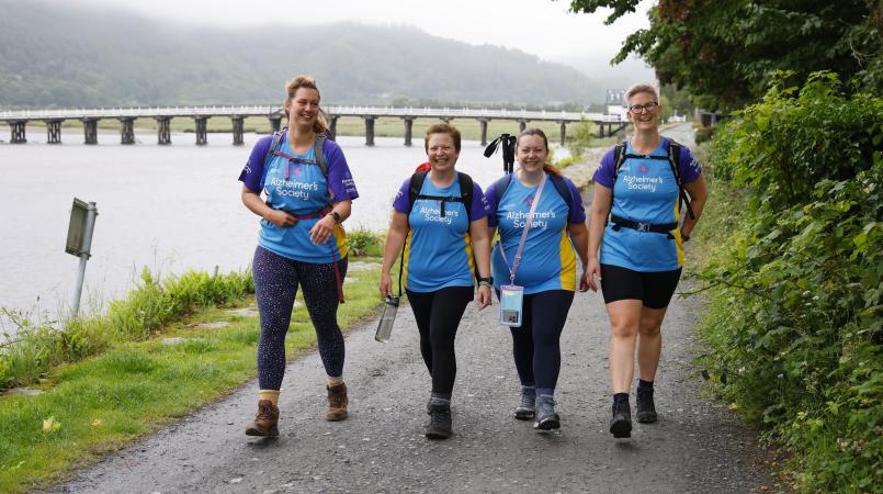 Four women walking on a path with an bridge in the background.