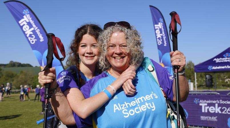 Two women smiling in front of Trek26 flag in a field.